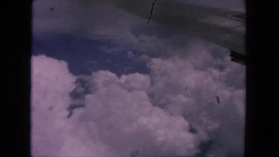 1962 8mm view from an airplane window over cloud tops, with no people or markings visible.