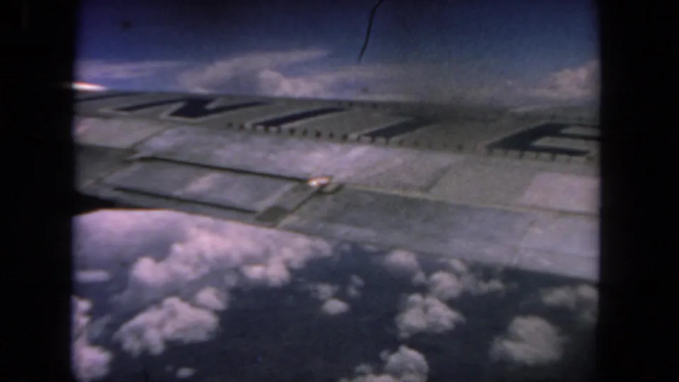 1962 8mm passenger-window view near San Diego with the airplane wing and dark striping above scattered clouds.