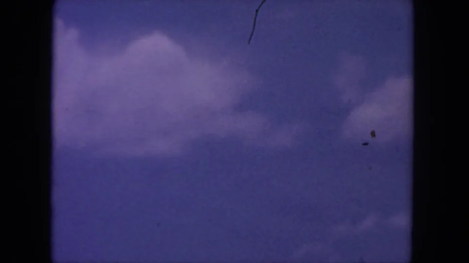 1962 8mm home-movie frame from San Diego metadata showing purple-blue sky, soft clouds, gate edges, dust, and a visible scratch.