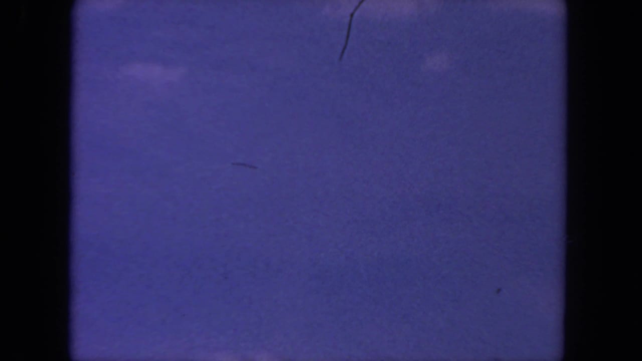 1962 8mm home-movie frame from San Diego metadata showing a mostly open purple-blue sky with faint clouds and visible film gate edges.