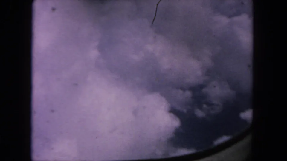 1962 8mm home-movie frame from San Diego metadata showing billowing white and gray clouds under a purple sky, with dust and frame edges.