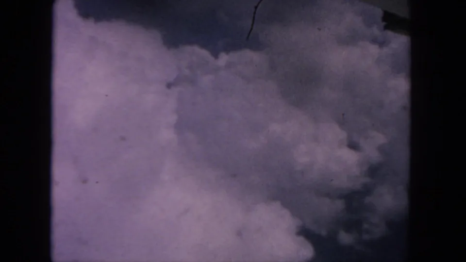 1962 8mm home-movie frame from San Diego metadata showing dense clouds against a purple-tinted sky with dark gate edges and surface marks.