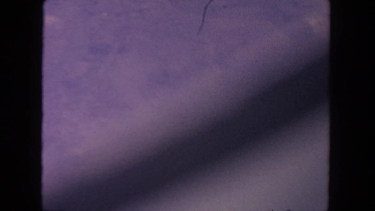 1962 8mm San Diego sky view with violet-blue clouds, film gate edges, and a diagonal shadow crossing the frame.