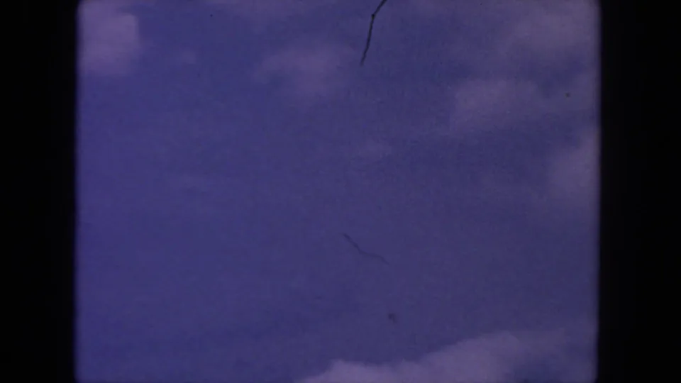 1962 8mm San Diego sky frame with faint cloud forms, blue color shift, gate borders, and visible surface wear.