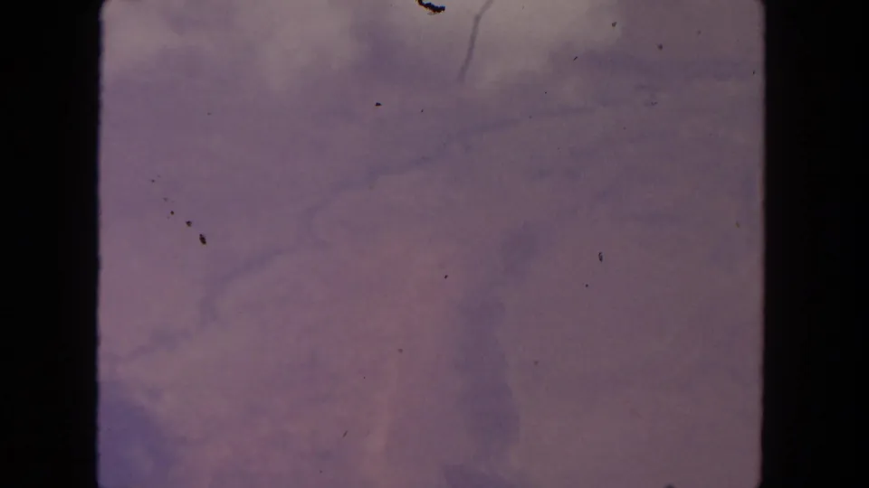 1962 San Diego-area aerial home-movie frame showing soft haze, faint terrain or cloud texture, scratches, and dark film edges.