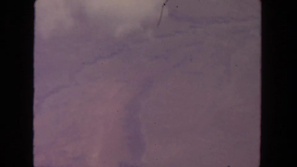 Final 1962 8mm aerial frame with pink-purple haze, faint clouds, dust, scratches, and no visible people or structures.