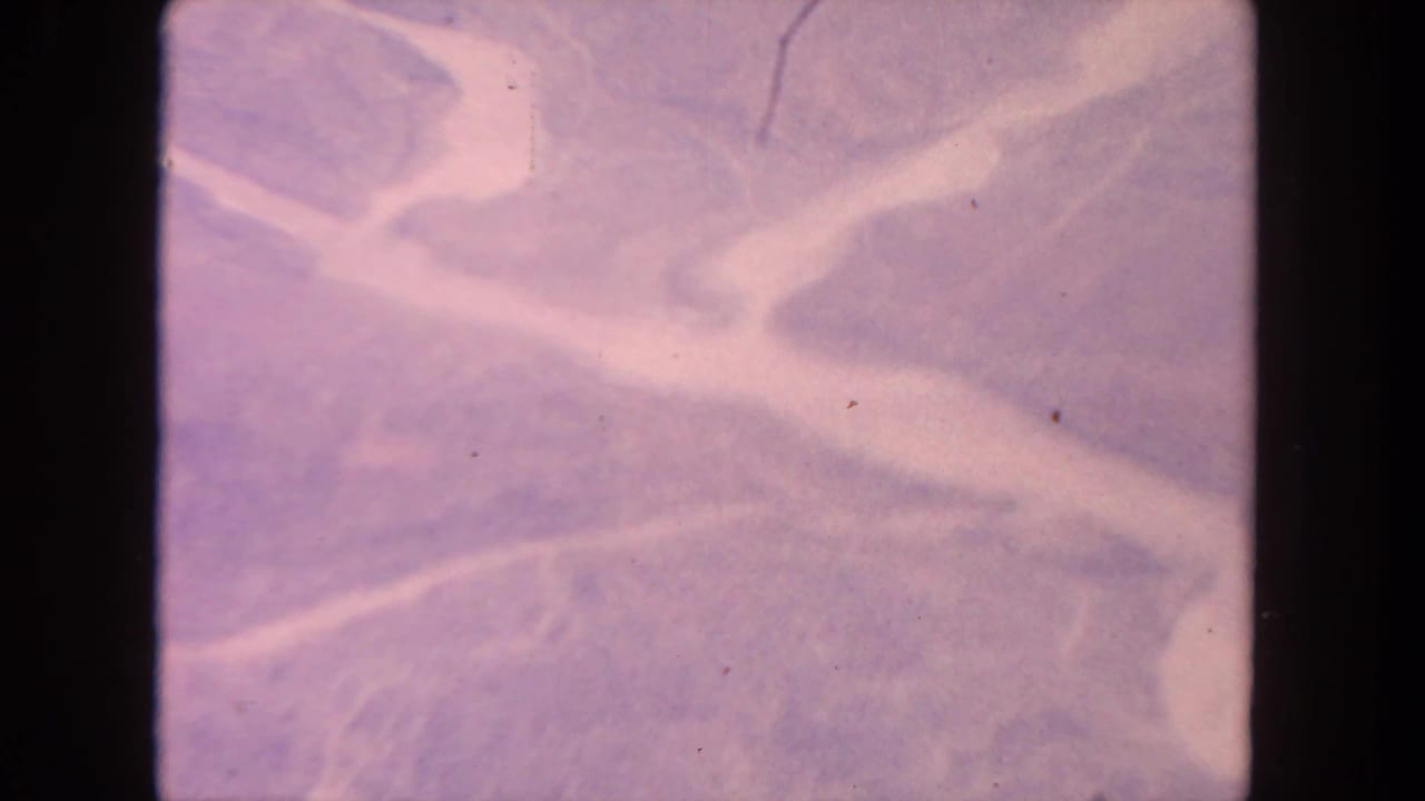 1962 San Diego-area 8mm frame with bright winding waterways crossing pink-lavender terrain and visible film scratches.