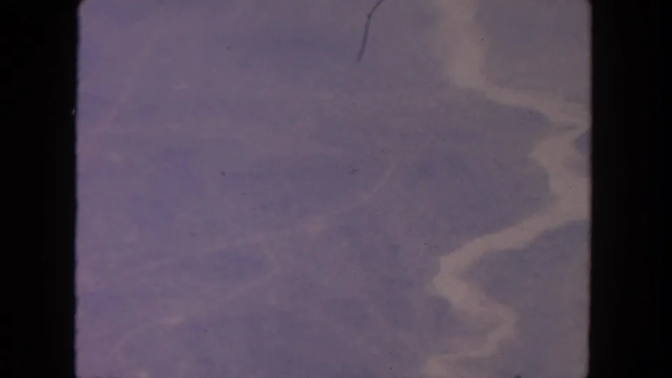 1962 San Diego-area 8mm frame with dim purple-blue terrain, faint pale water shapes, and rounded black film borders.