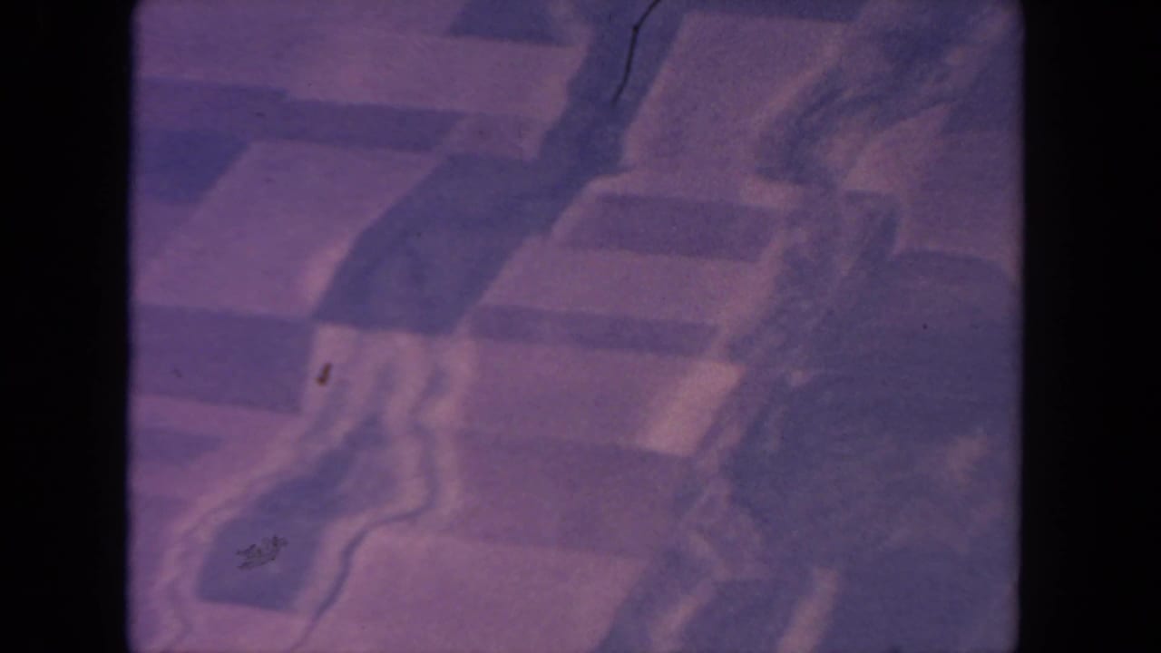 1962 8mm aerial view, likely over San Diego, with indistinct city blocks, road lines, heavy purple tint, grain, and gate borders.
