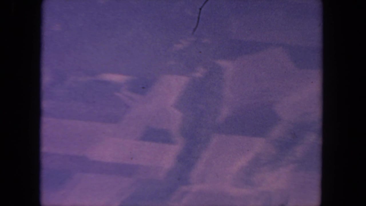 Likely San Diego aerial frame from 1962 showing blurred streets and block shapes with 8mm grain, scratches, and dark frame edges.