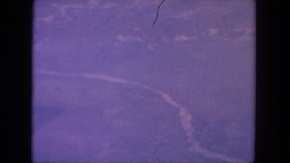 Likely San Diego 1962 aerial frame with a curving pale line, indistinct terrain, grain, scratches, and 8mm frame borders.