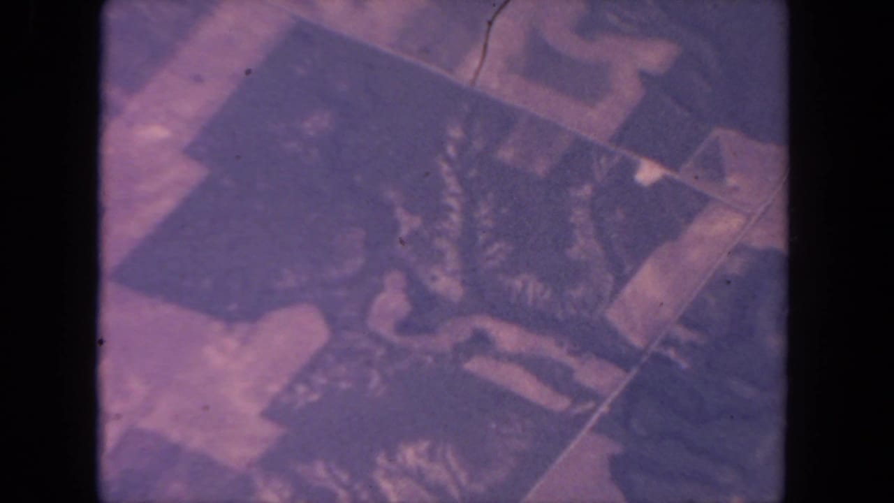 Soft aerial view of patchwork fields with magenta and navy film color shift.