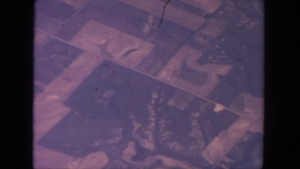 1962 San Diego 8mm frame showing blurred aerial terrain with pale dividing lines, dark patches, and visible film wear.