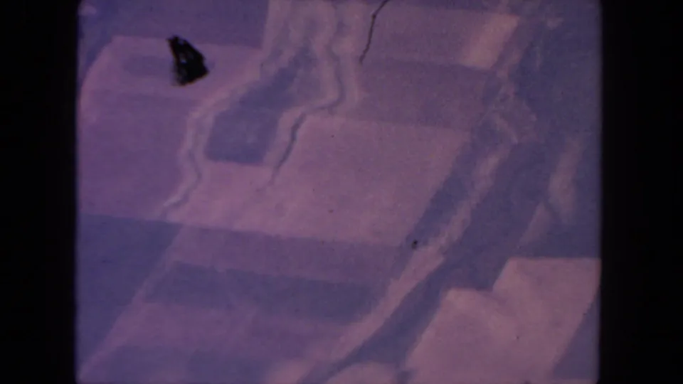 1962 San Diego aerial frame with winding pale lines, blocky terrain shapes, purple-pink cast, and a dark film mark near center.