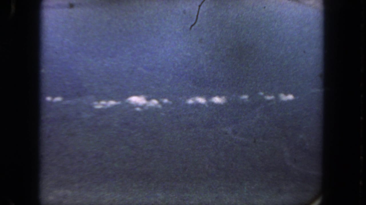 Blue-tinted 8mm frame from the San Diego clip, with heavy grain, dark borders, and an indistinct line of white highlights across the scene.