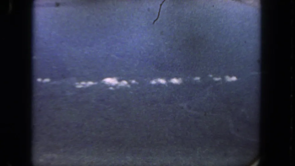 Blue-tinted 8mm frame from the San Diego clip, with heavy grain, dark borders, and an indistinct line of white highlights across the scene.