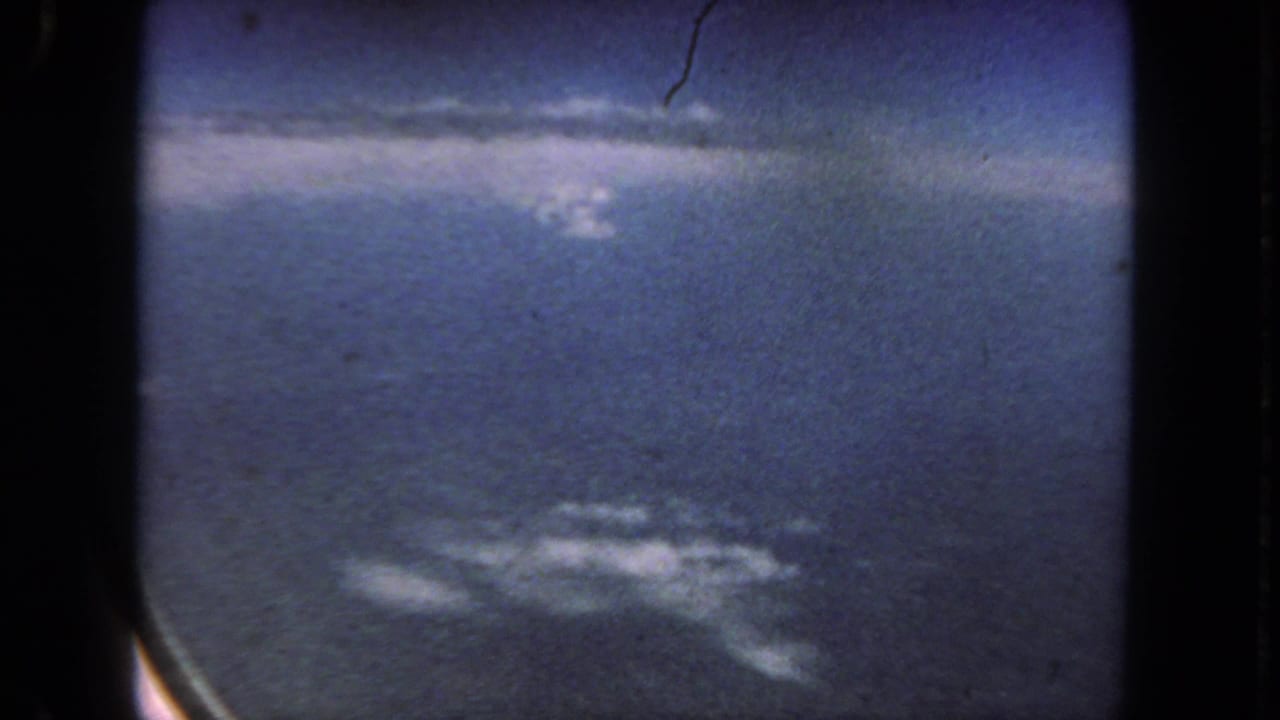 1962 8mm home-movie frame from a flight near San Diego, showing blue sky and small clouds through an airplane window.