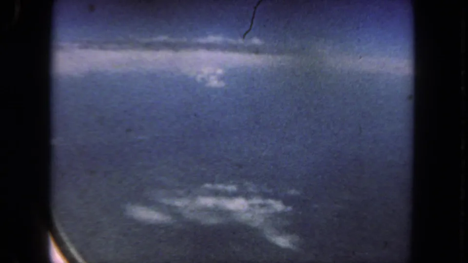 1962 8mm home-movie frame from a flight near San Diego, showing blue sky and small clouds through an airplane window.