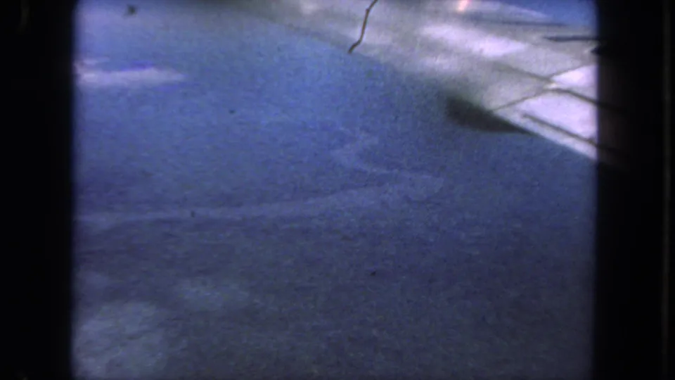 1962 San Diego home-movie frame with blurred pavement, a pale road edge, dark frame borders, and small film marks.