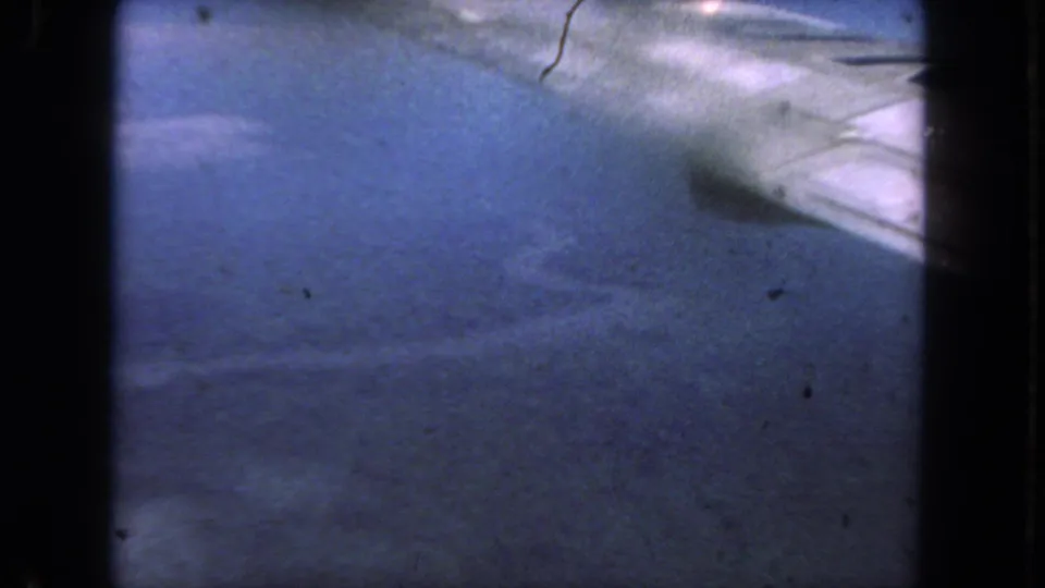 1962 San Diego 8mm still showing grainy blue pavement, light streaks, frame borders, and marks from the film scan.