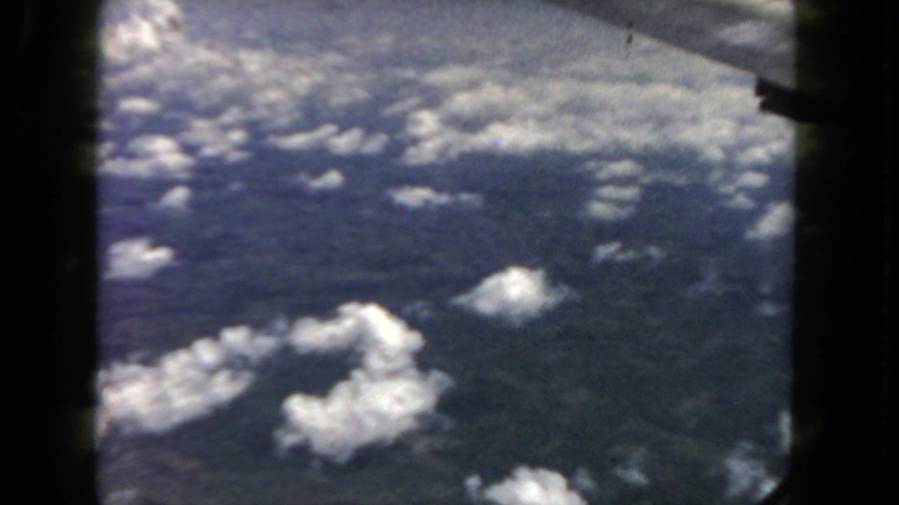 Clouds and blue sky seen through a dark airplane window frame.