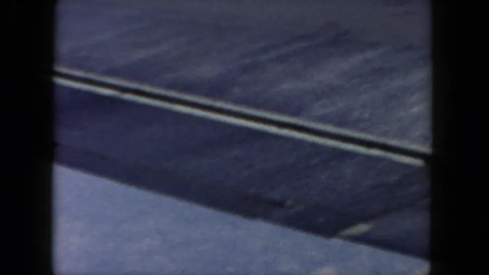 1962 8mm home-movie frame from a passenger window, showing an airplane wing against blue sky with dark frame borders.