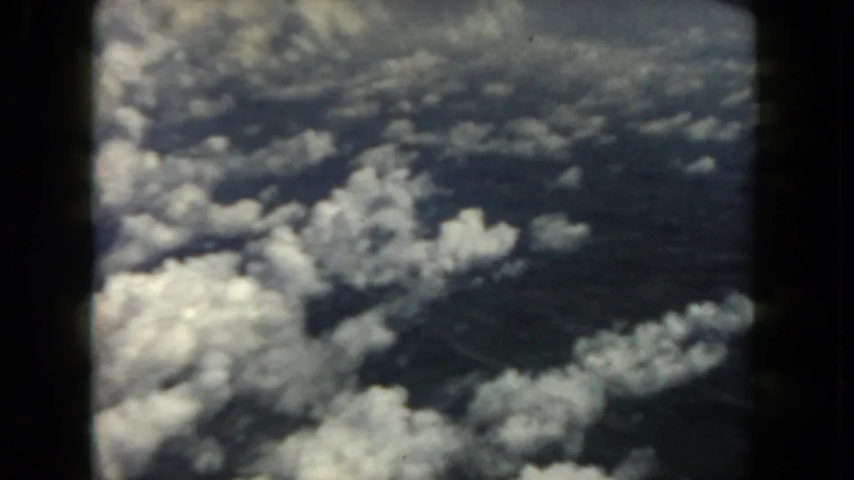 1962 home-movie aerial frame showing scattered clouds over indistinct ground, bordered by dark window or film edges.