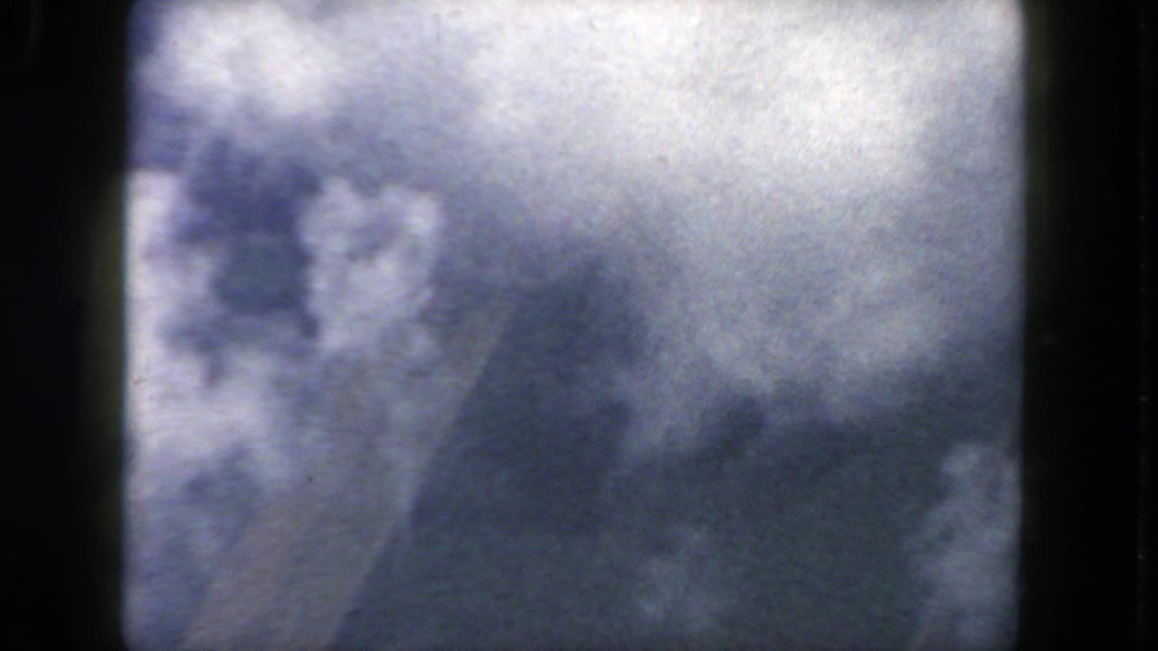Clouds seen through dark airplane window framing.