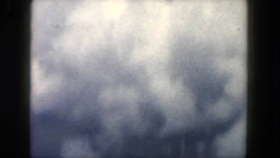 1962 in-flight home-movie view with cloud layers and a partial airplane wing visible beyond the dark window frame.