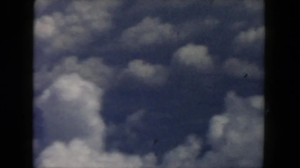 1962 8mm passenger perspective on darker cloud formations below the airplane window frame.