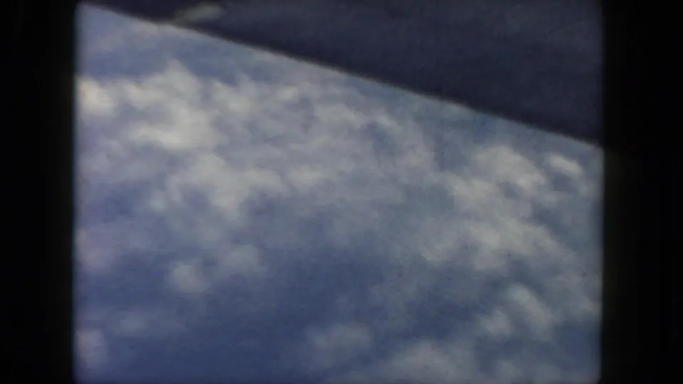 1962 home-movie frame showing an airplane wing over a broad cloud layer through the window.