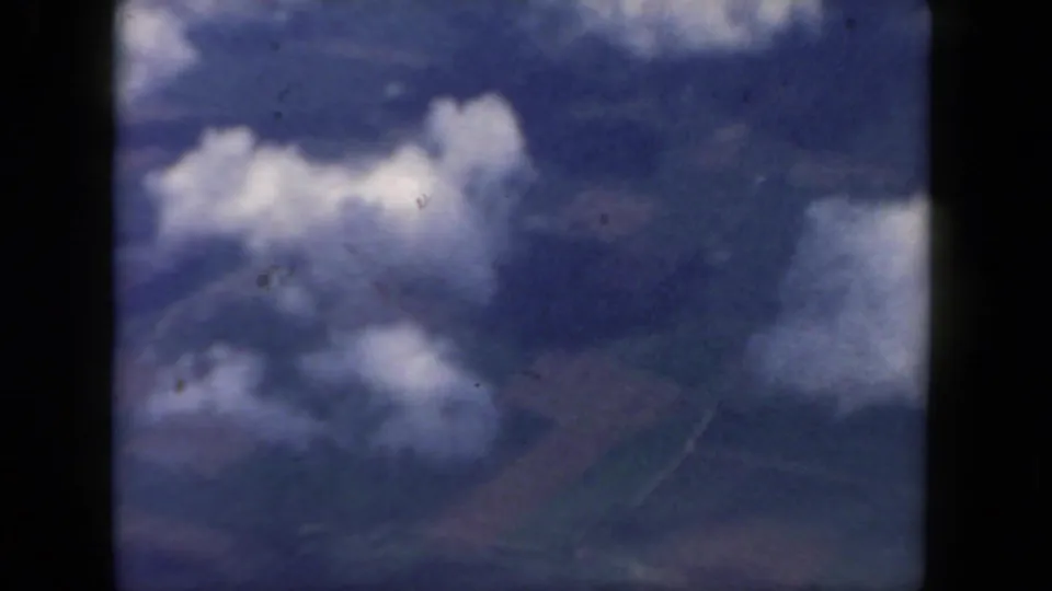A soft 8mm aerial view shows clouds and blue haze from an airplane-window perspective.