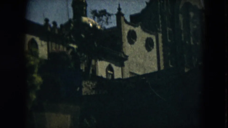 1962 Mexico City home-movie frame showing a white church facade partly hidden by trees and shadow.