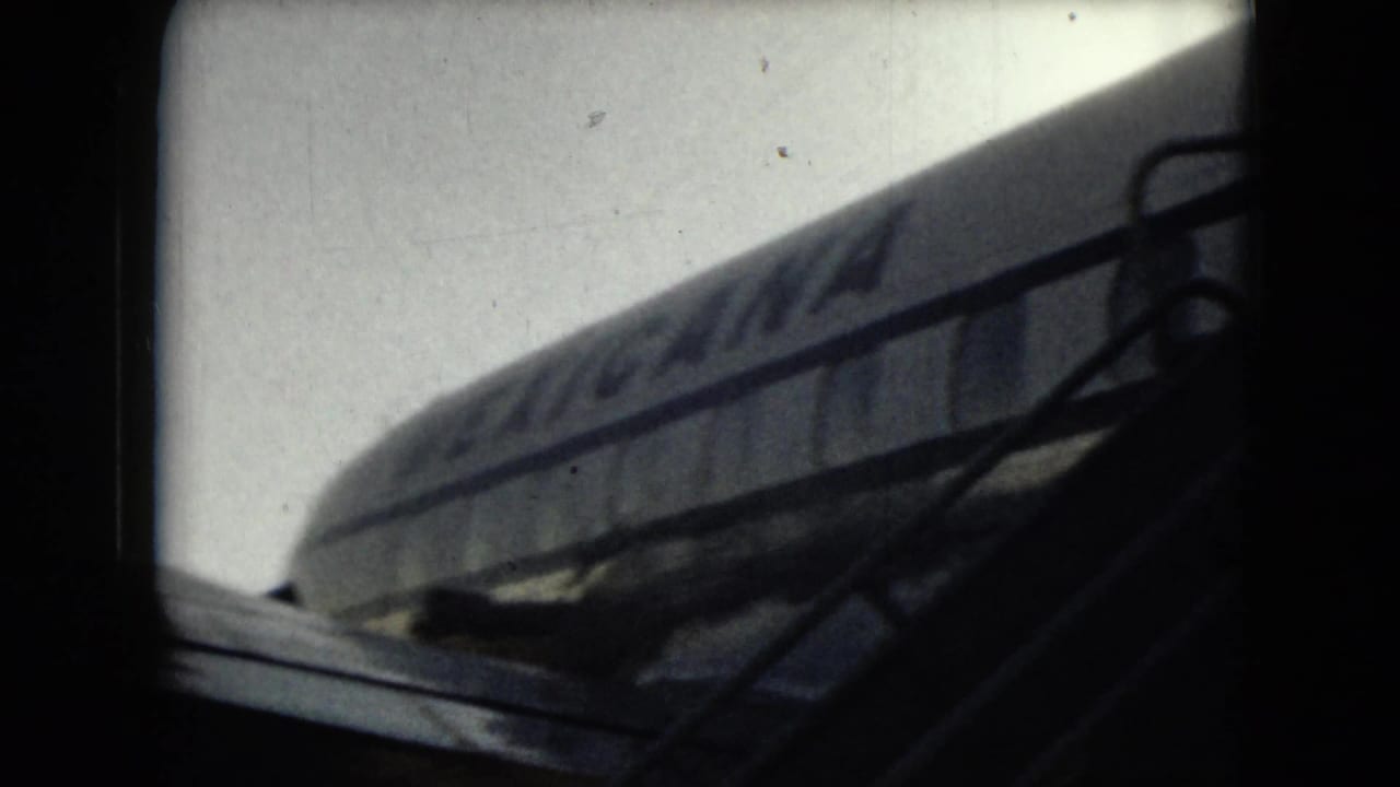 1962 Mexico City travel footage shows a parked airliner seen from a dark terminal or window-side vantage point.