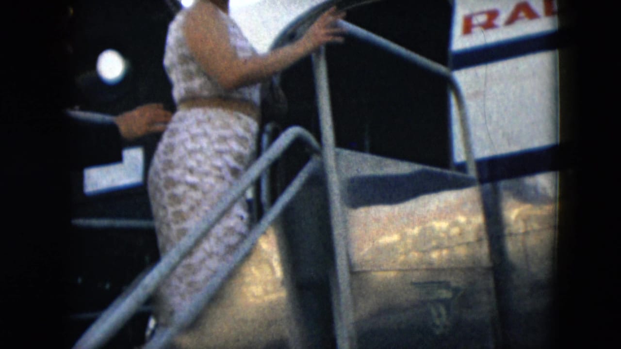 Woman climbs mobile stairs beside an aircraft fuselage with partial lettering visible.