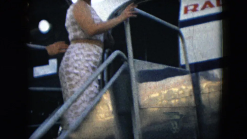 A woman in a patterned dress climbs mobile stairs beside a Mexicana aircraft fuselage in 1962 Mexico City footage.