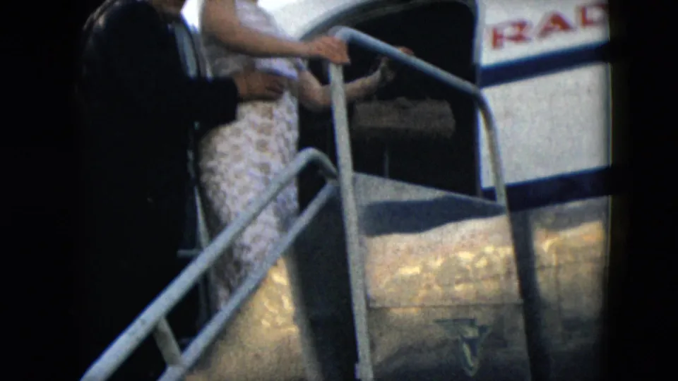 A close 8mm view shows the woman and suited man on aircraft stairs, with partial Mexicana lettering on the fuselage.