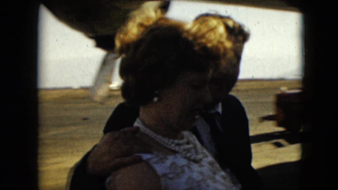 Couple in formal clothes walking beside a propeller plane on a sunlit tarmac.