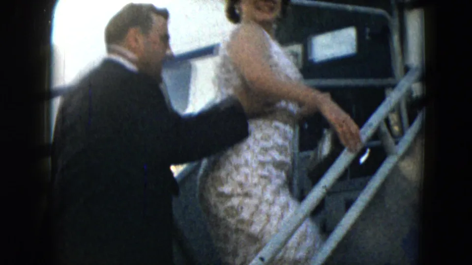 1962 Mexico City home-movie frame showing a suited man following a woman in a white dress up the stairs into a plane.
