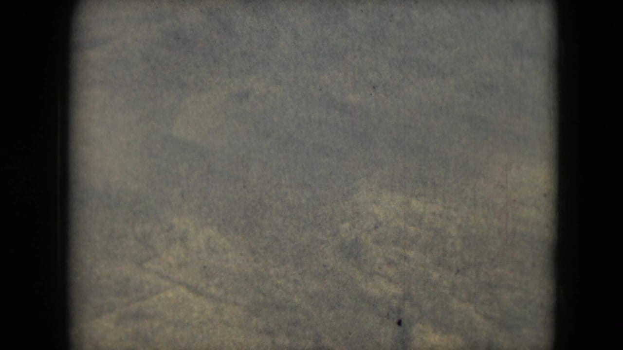 Faint hazy terrain seen within a dark 8mm film frame border.