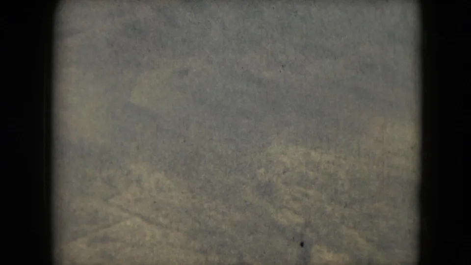 1962 8mm frame with muted, indistinct earth-toned terrain and heavy grain, bordered by dark film edges.
