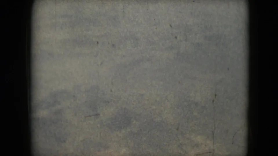 Muted 1962 8mm view of indistinct barren terrain with visible grain, scratches, and a dark vertical frame edge.