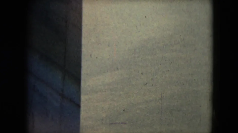1962 8mm frame with pale barren terrain, a dark vertical film or shadow band, grain, and fine scratches.