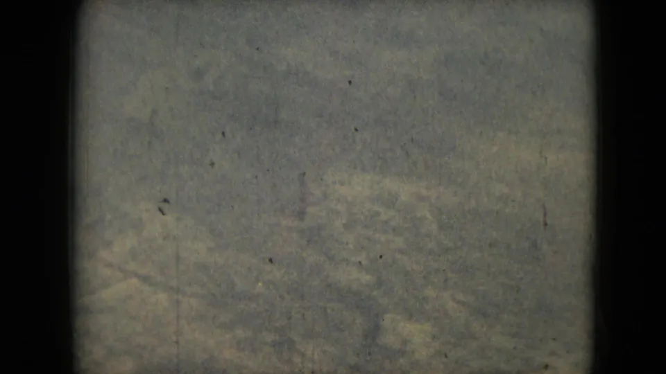 Abstract Mexico City 1962 8mm frame with gray-green mottled texture, visible grain, small dust marks, and a dark border at the edge.