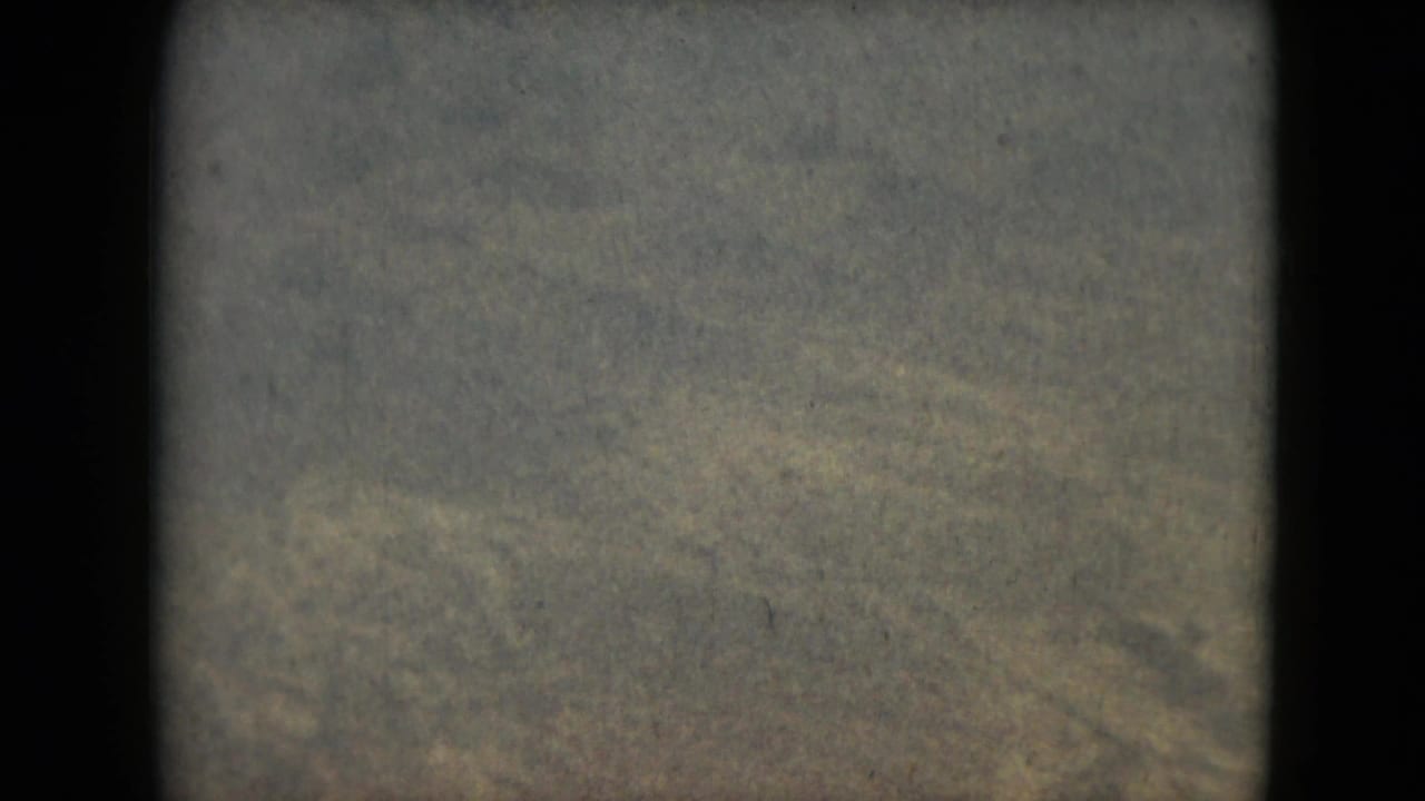 Soft aerial view of pale snowy mountain terrain with dark film borders and grain.