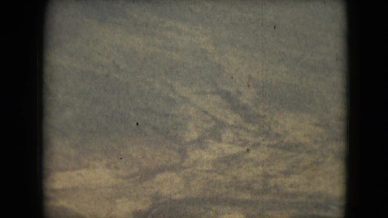 Aerial snowy terrain with faint ridges, muted exposure, and vertical film border.