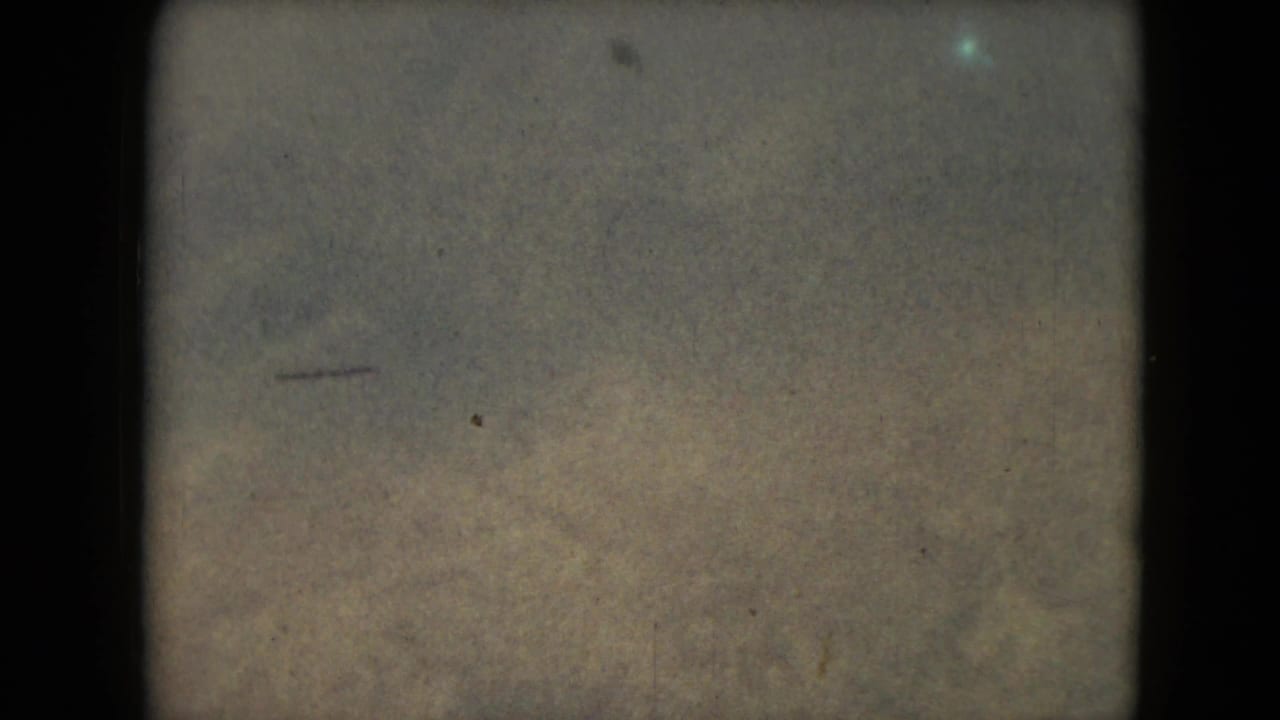 1962 8mm frame from Mexico metadata showing muted mountain terrain beneath a hazy sky with heavy film borders and grain.