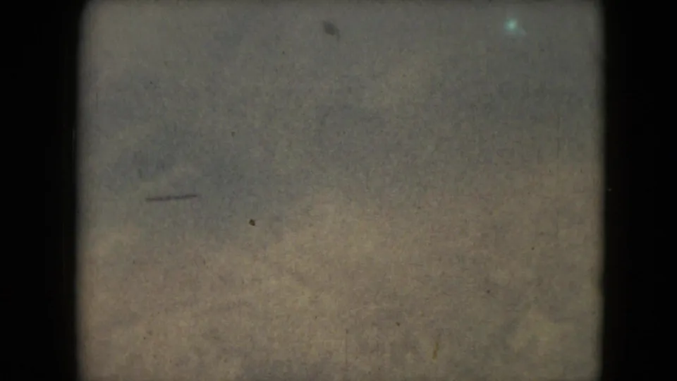 1962 8mm frame from Mexico metadata showing muted mountain terrain beneath a hazy sky with heavy film borders and grain.