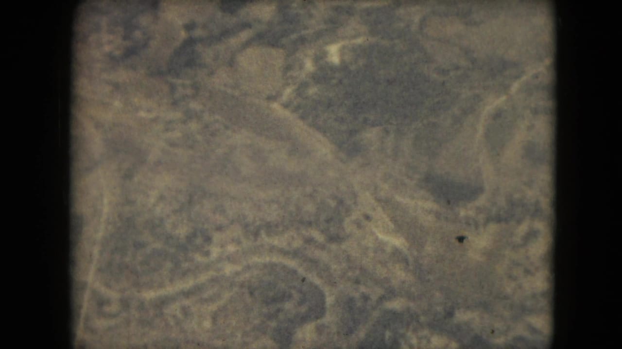 Grainy 1962 8mm overhead view associated with Mexico City metadata, showing rugged tree-covered ground and faint roadlike lines.