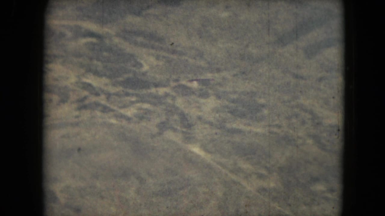 Aerial view of dry, scrubby terrain with pale winding ground lines and faded film color.